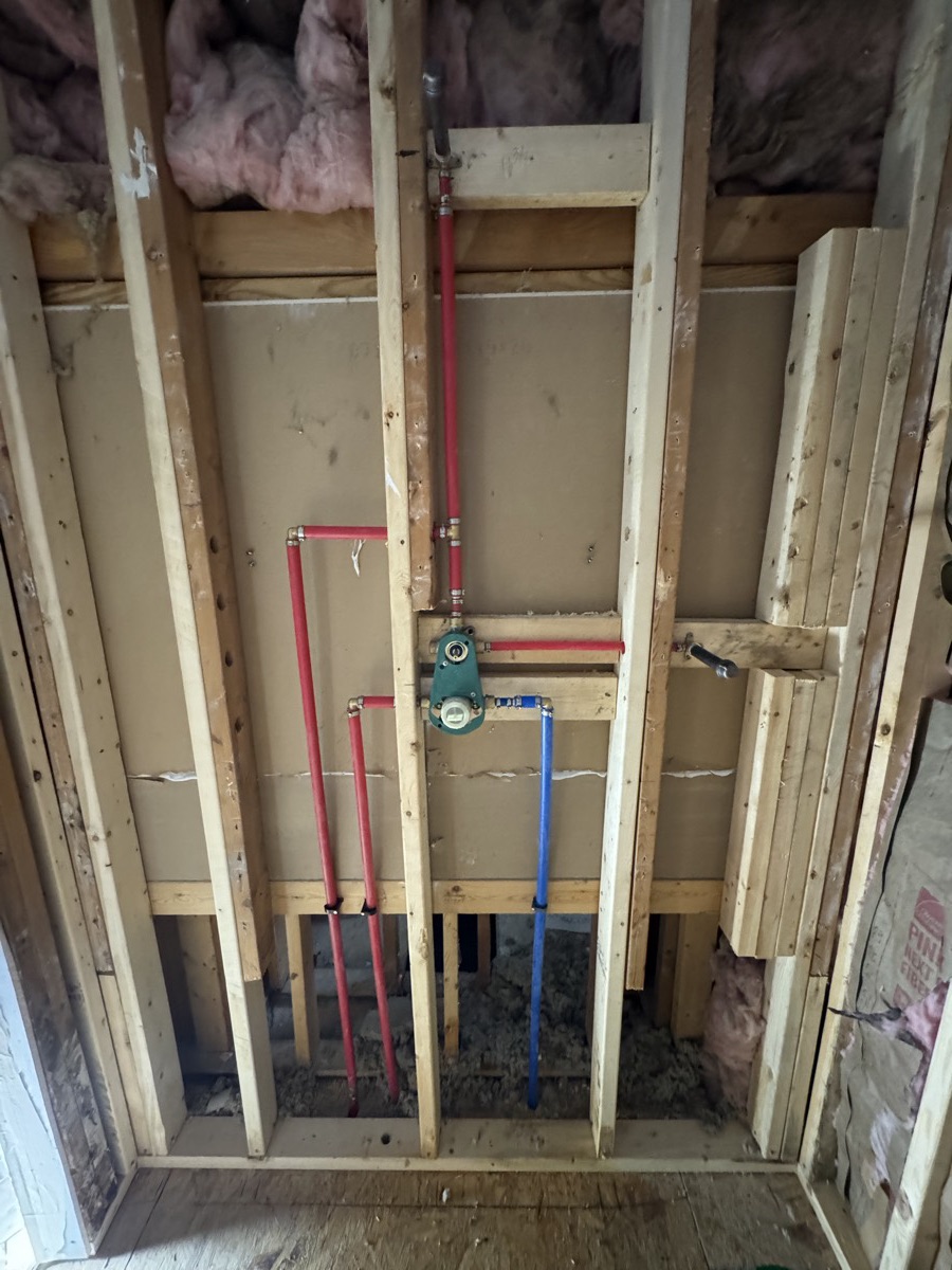 New red and blue water lines and a shower valve installed in open wall framing