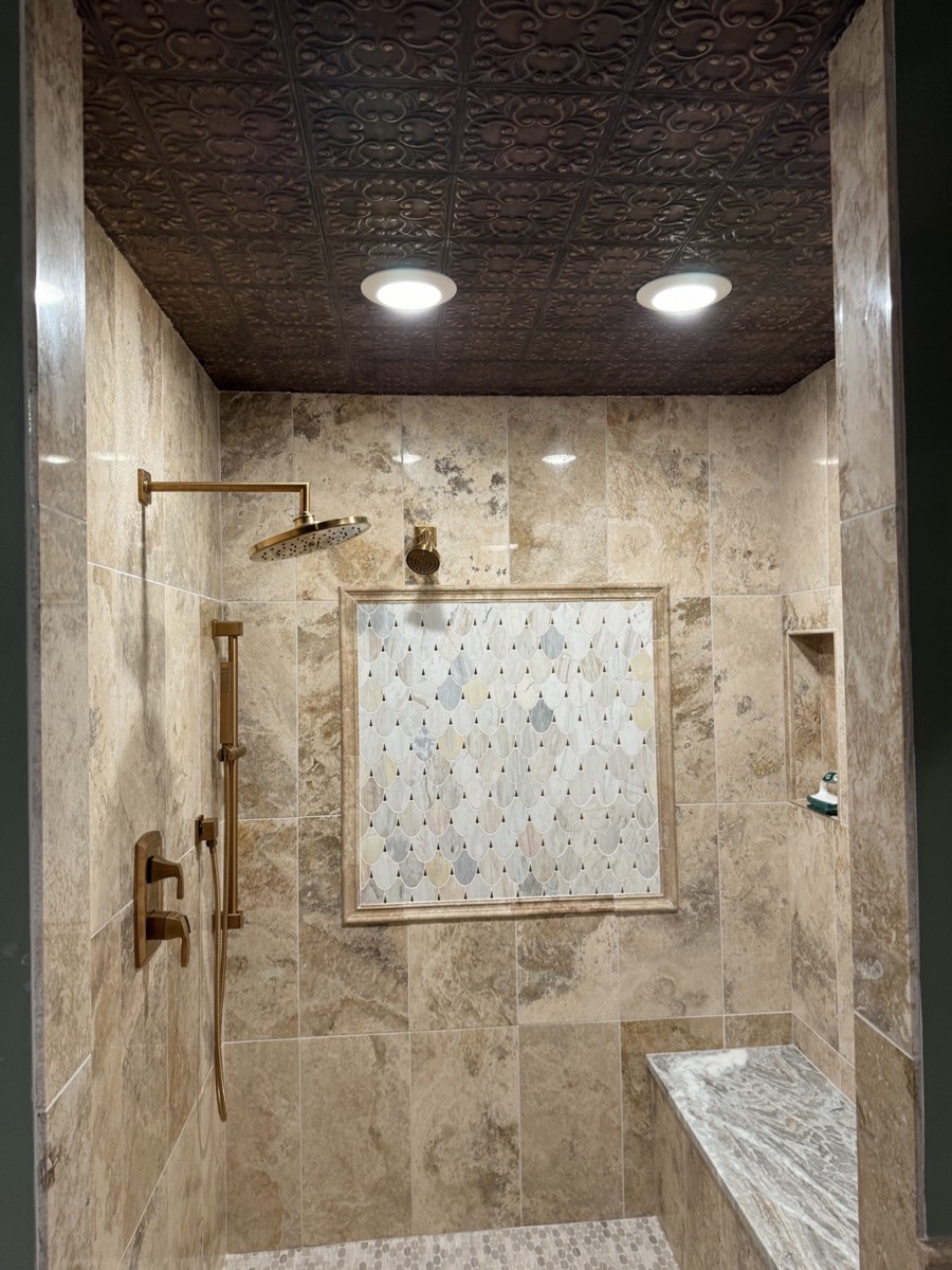 Travertine walk-in shower with warm gold-tone shower fixtures, a mosaic medallion and a built-in bench in West Alexandria, OH