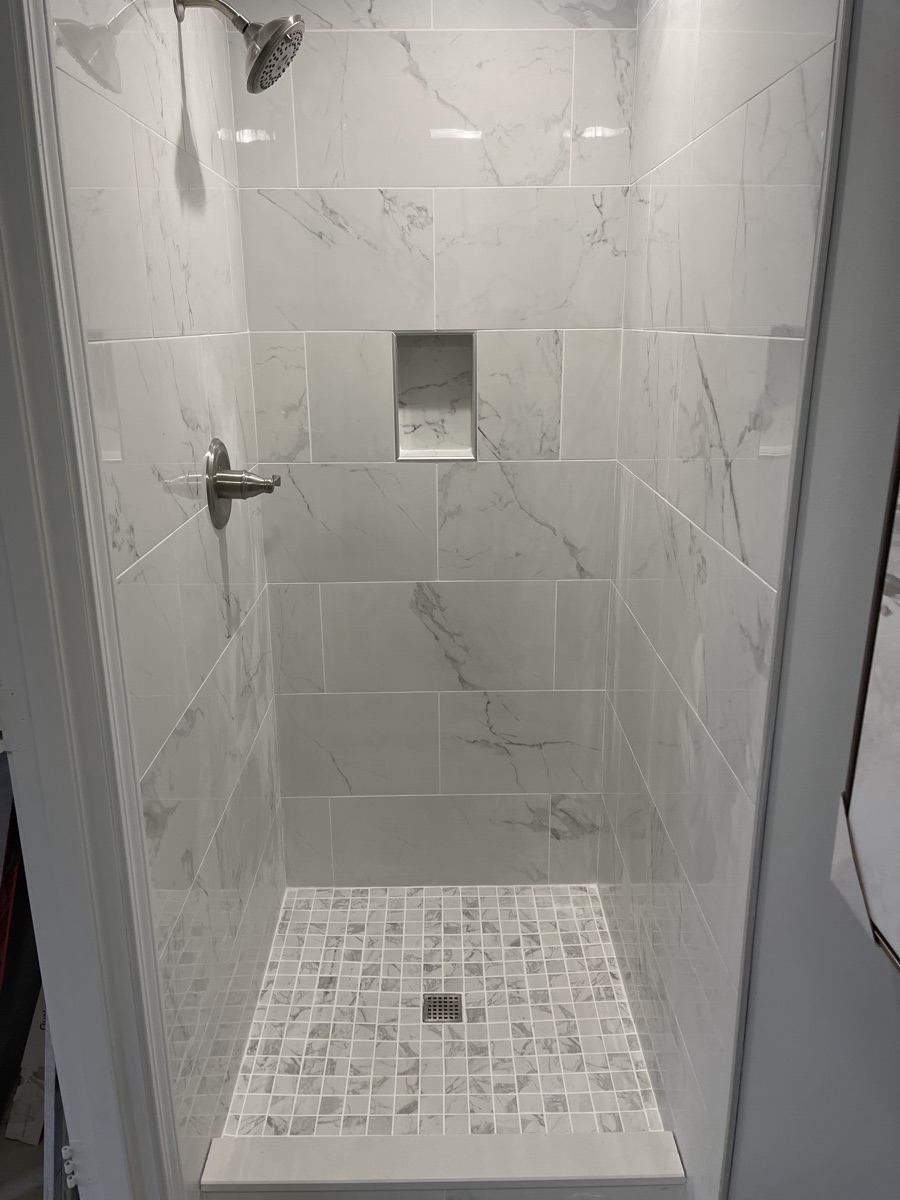 White marble-look tile walk-in shower with a built-in niche and mosaic floor in Springboro, OH