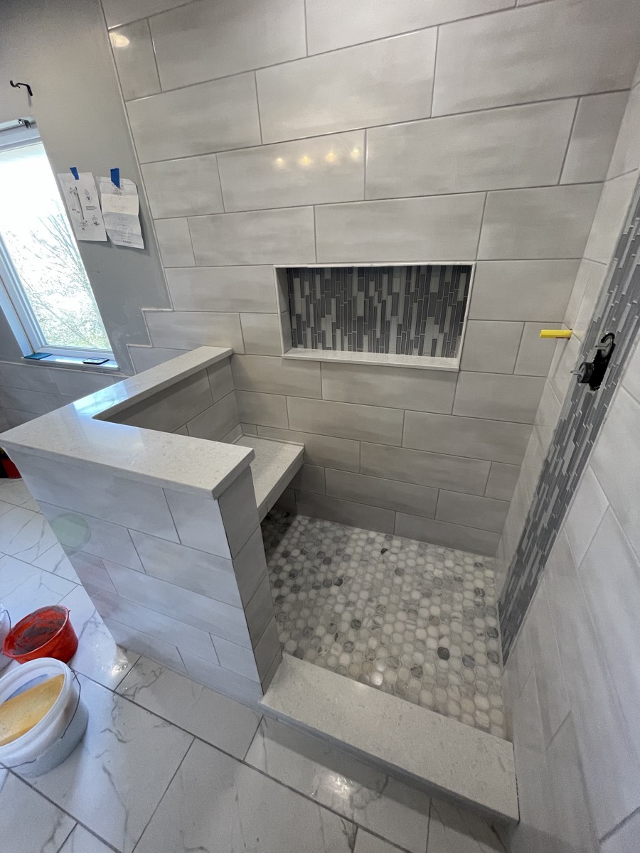 Tile shower with a built-in bench, mosaic floor and a long tile niche