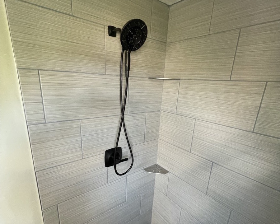 Tile shower walls with built-in corner shelves and a matte black valve and handheld shower