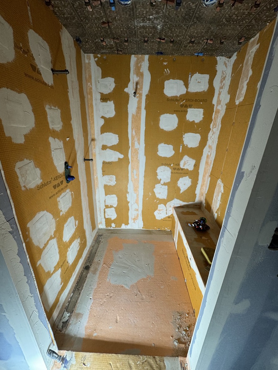 Shower walls, niche and bench covered in orange waterproofing membrane before tile