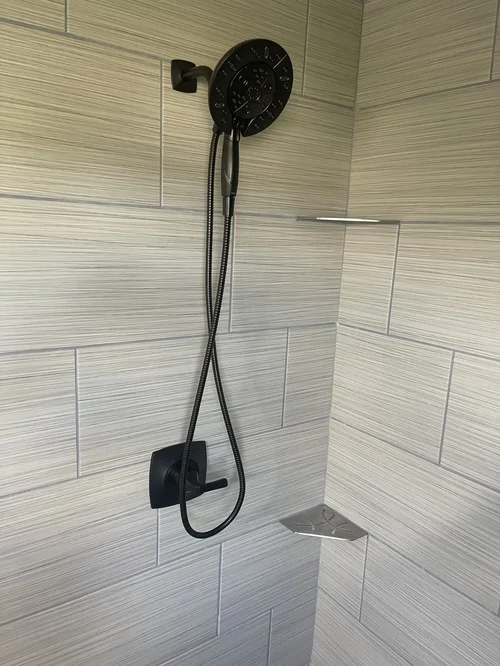 Black shower head with a handheld hose mounted on a tiled bathroom wall
