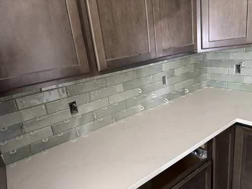 Kitchen backsplash under construction with green subway tiles and exposed electrical outlets